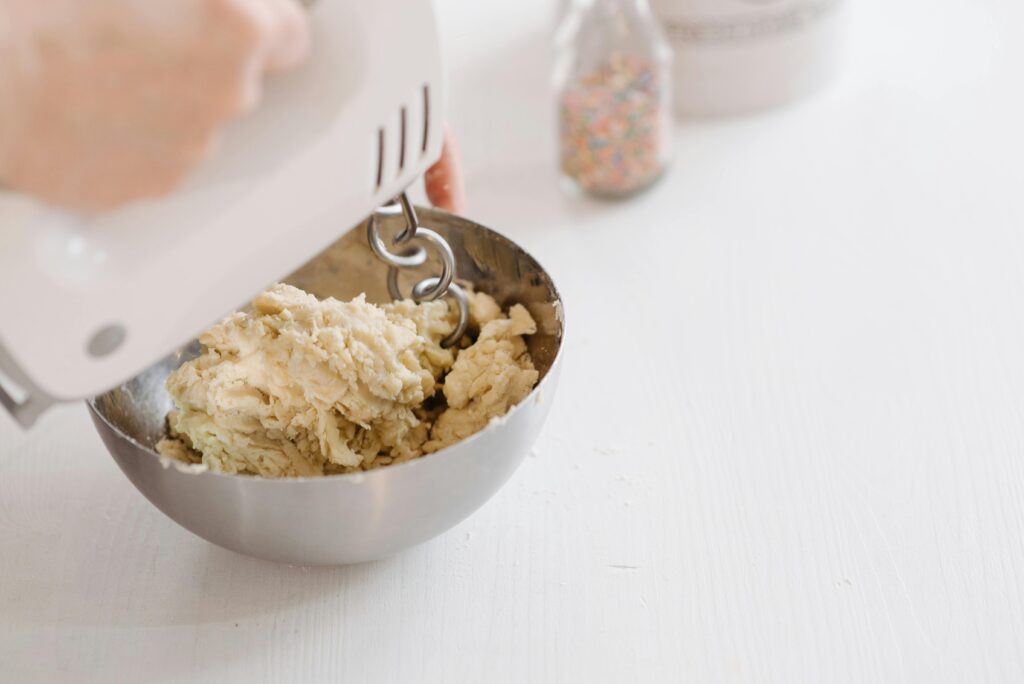 Close-up of dough being mixed in a stainless steel bowl with an electric mixer.